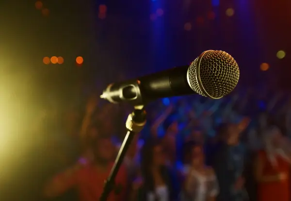 Close-up de um microfone em um palco iluminado, com uma plateia ao fundo durante um show de música gospel.